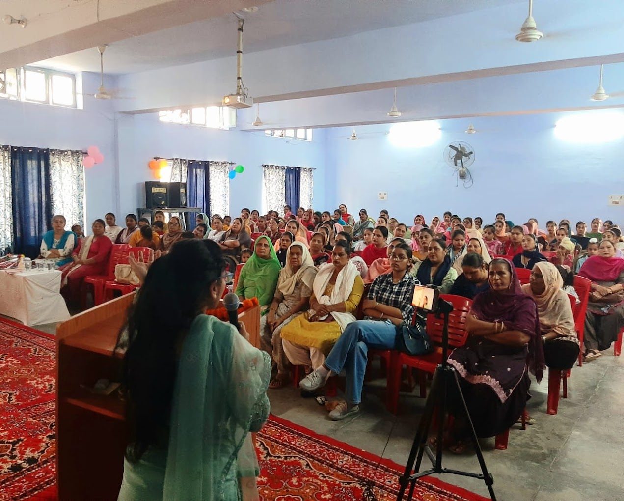 Dr. Kaushal addressing a seated audience of teachers and parents in a hall