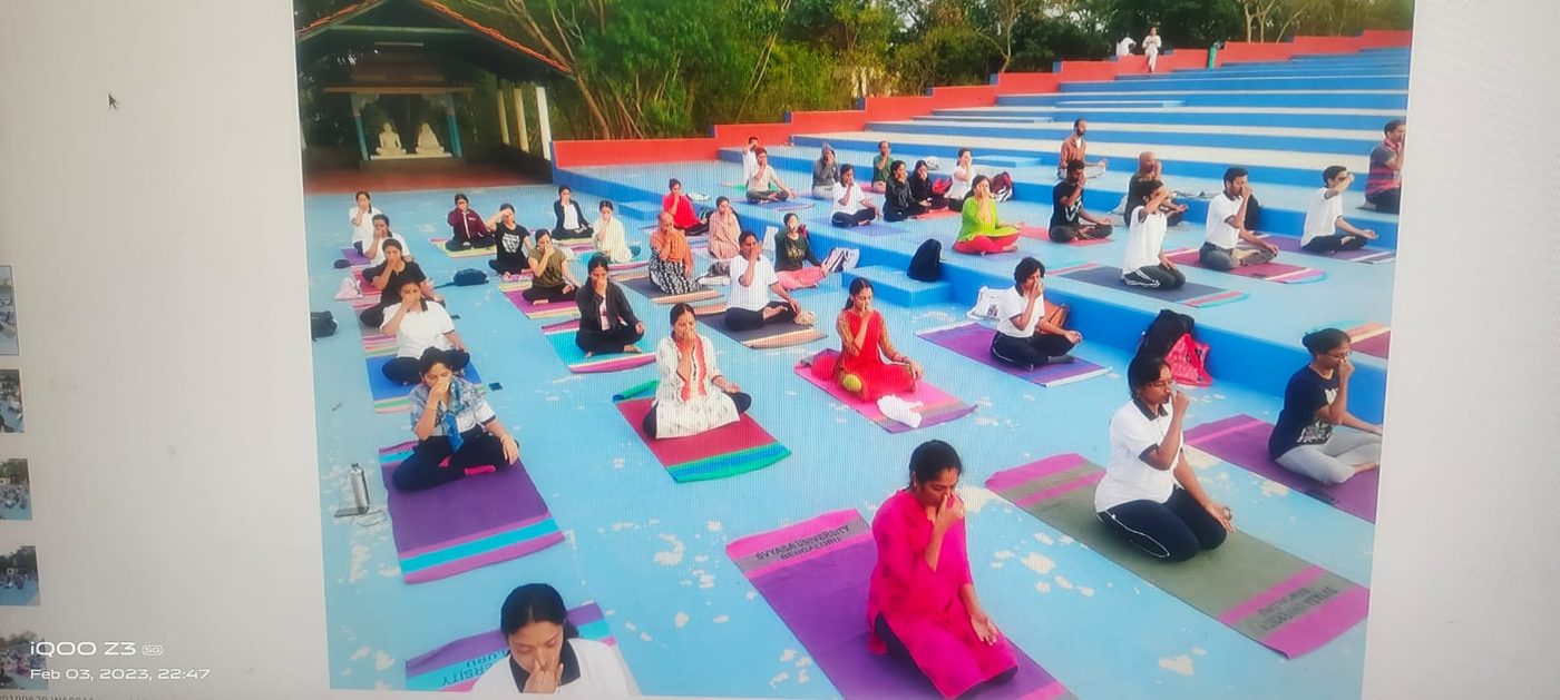 A large outdoor yoga class seated on colourful mats on tiered steps